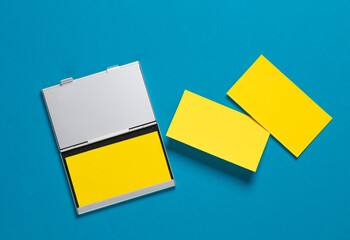 Metal box business card holder with yellow business cards on blue background