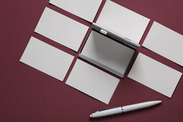 Metal box business card holder with business cards and pen on burgundy background. Top view