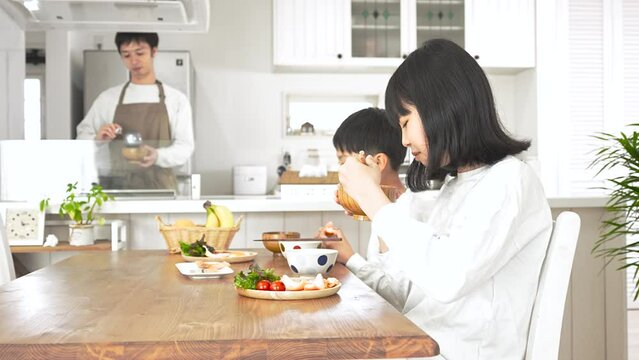 自宅で朝食を食べる子供と料理をしている男性