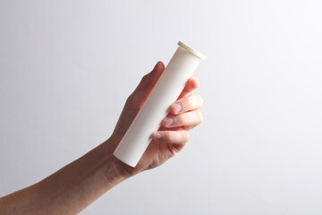 Hand in denim shirt holding pills tube on gray background