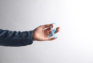 Male hand in denim shirt holding blue prostate cancer awareness ribbon on gray background