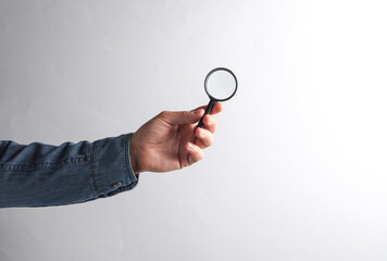 Man's hand in denim shirt holding magnifier glass on gray background
