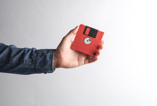 Man's hand in denim shirt holding red floppy disk on gray background