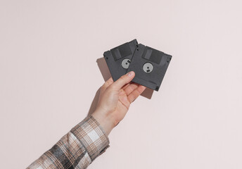 Man's hand in shirt holding black floppy disks on beige background with shadow