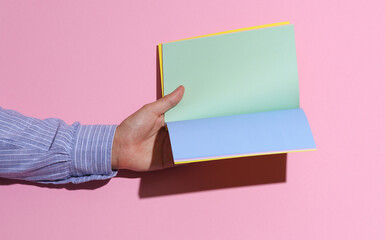 Man's hand in shirt holding open notebook on pink background with shadow
