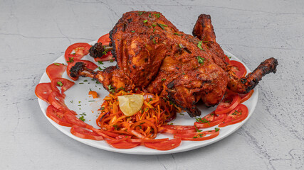 Homemade Indian tandoor cooking- tandoori chicken with vegetable salads and onion at plate on textured background
