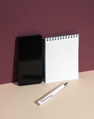 Smartphone, White notebook with pen on burgundy beige background. Creative layout