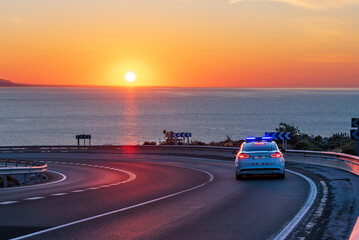 Highway police patrol car driving along the sea at dawn.