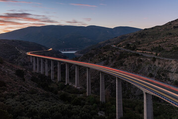 Long bridge in a valley and over a swamp at dawn, with the beams of light from the vehicles passing over the road, long exposure.