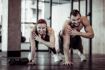 Fototapeta na wymiar Athletic smiling couple man and woman do push-ups together in the gym. Healthy lifestyle