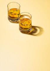 Two whiskey glasses with ice cubes on golden background.