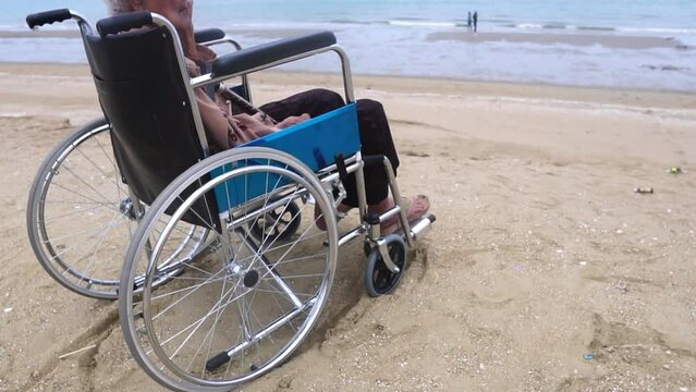 Fotage Slow Motion: Senior asian woman siting on wheelchair looking out on Beach