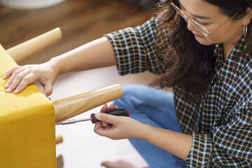 Obraz na płótnie Canvas Asian Woman self repairs furniture renovation using equipment to diy repairing furniture sitting on the floor at home