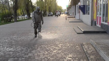 Man in protective suit spraying antiseptic solution on sidewalk in city. Persona disinfecting spray chemicals to preventing spread coronavirus. Sanitary measures in public place. Coronavirus pandemic