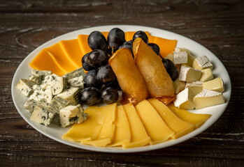 Delicious cheese plate decorated with caramel pear and grapes 