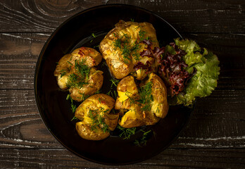 Baked potato on the black plate decorated with green dill and lettuce