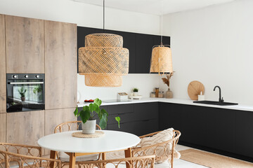 Interior of light kitchen with built-in oven, dining table and dark counters
