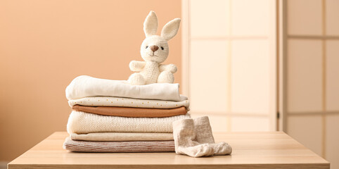 Stack of clean baby clothes, socks and bunny toy on table in room