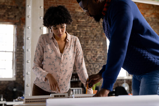 Focused diverse male and female architects standing at desk discussing building model at office