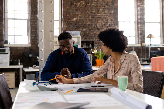 Focused diverse male and female architects discussing blueprints sitting at desk in office