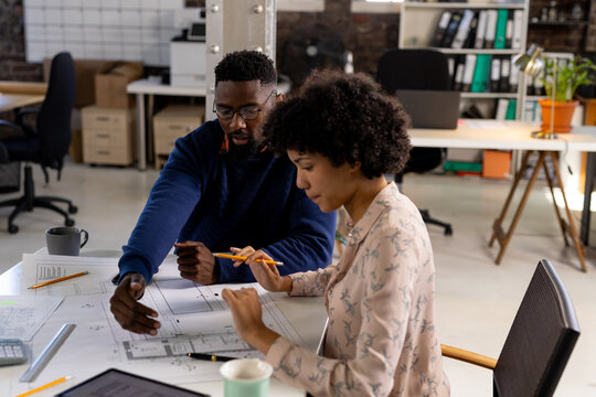 Focused diverse male and female architects discussing blueprints sitting at desk in office