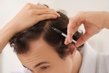 Fototapeta premium Young man with hair loss problem making injection in bathroom, closeup