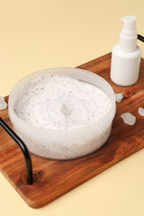 Wooden board with jar of body scrub and cosmetic product on color background, closeup