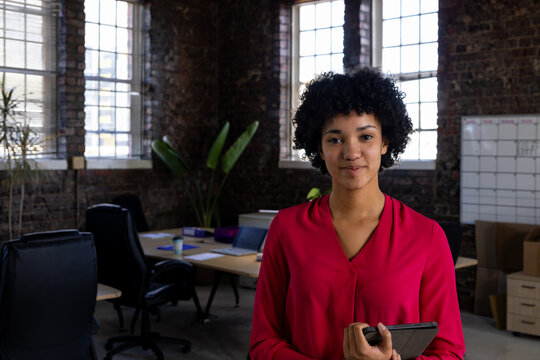 Portrait of happy biracial casual businesswoman holding tablet at office, copy space - Powered by Adobe