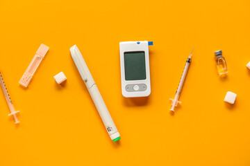 Glucometer with lancet pen, insulin and syringes on orange background. Diabetes concept