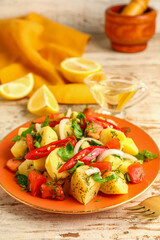 Plate of tasty Potato Salad with vegetables on light wooden background