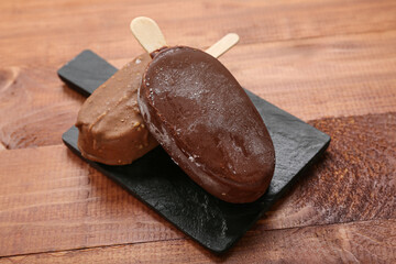 Board with tasty chocolate covered ice cream on wooden background