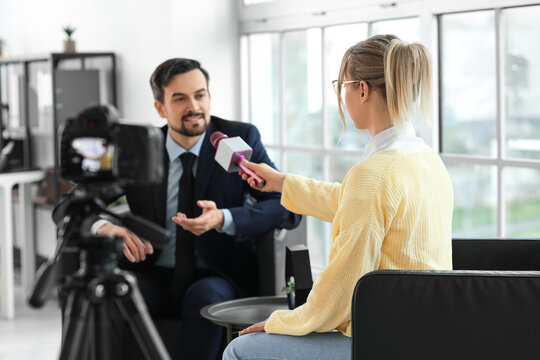 Female journalist with microphone having an interview with man on camera screen in office, closeup