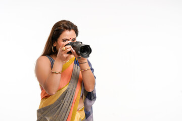 Indian woman in traditional sari and using camera on white background.