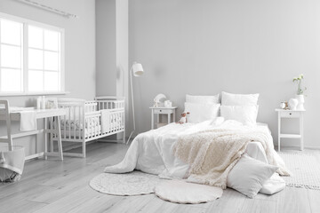 Interior of light bedroom with bed, changing table and baby crib
