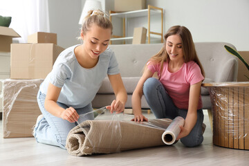 Young women wrapping carpet with stretch film at home