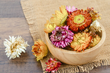 The Dried straw flower heads in wooden cup on wooden background.