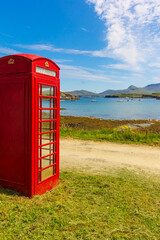 Portrait of a red, old fashioned telephone box overlooking yachts in the bay on the Isle of Canna, Small Isles, Scotland.  Copy Space, vertical.