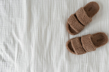 Fototapeta na wymiar Soft fluffy slippers on white muslin cloth. Flat lay, top view minimal fashion concept