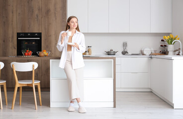 Happy young woman enjoying cup of coffee in modern kitchen