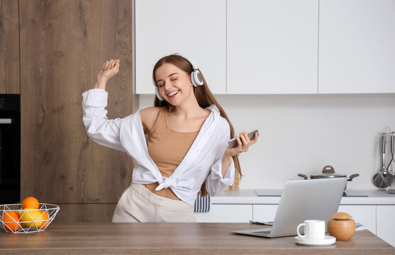 Happy Young Woman Listening To Music And Dancing In Modern Kitchen