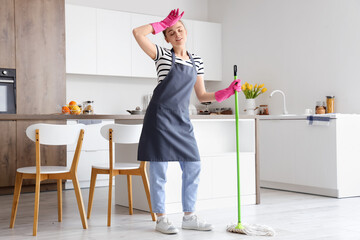 Tired young woman with floor mop in light kitchen