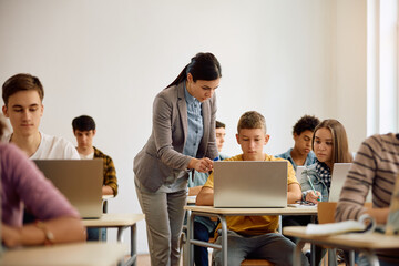 Female teacher assists high school student during computer class in classroom.