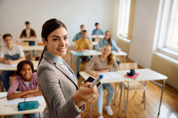 Happy teacher giving lecture to high school students in classroom.