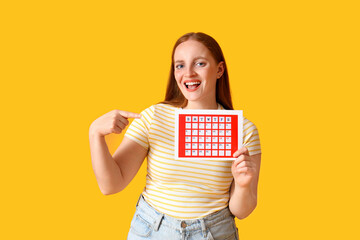 Young woman pointing menstrual calendar on yellow background