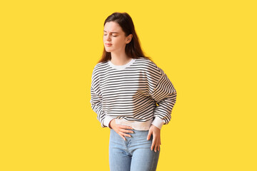 Young woman having menstrual cramps on yellow background