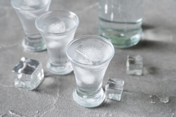 Shots and bottle of vodka with ice cubes on grey background
