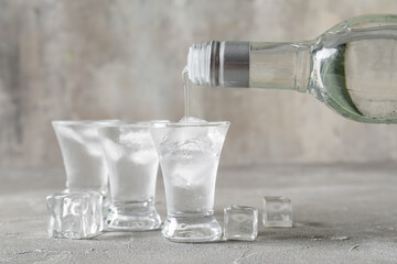 Pouring of vodka from bottle into shot on grey background