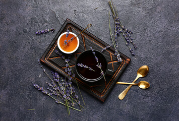 Bowl with sweet lavender honey and cup of tea on dark background
