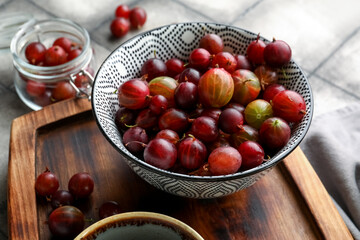 Bowl and jar with fresh gooseberries on grey tile background