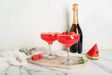 Board with glasses of tasty watermelon cocktail and champagne bottle on white grunge table